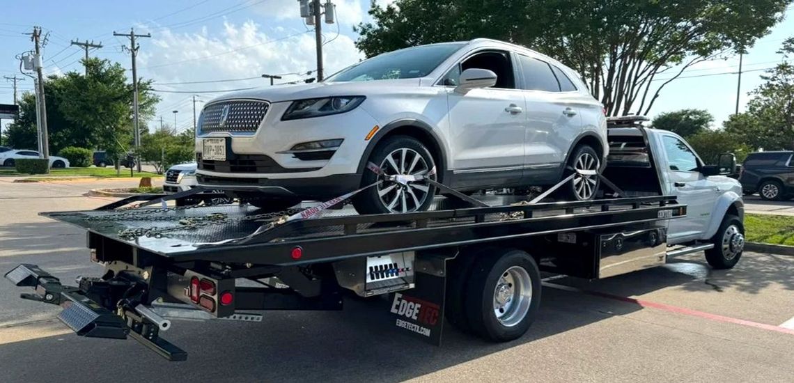 A silver Lincoln SUV being towed on a flatbed tow truck.