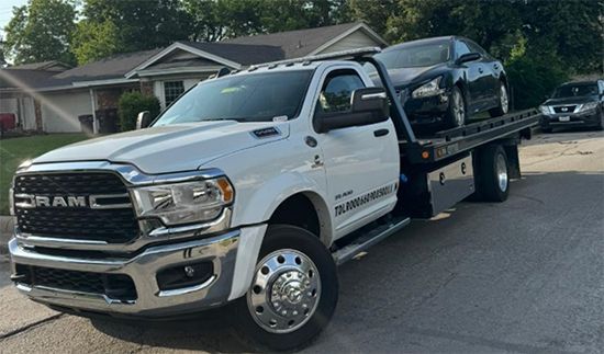 White tow truck carrying a black car on a residential street.