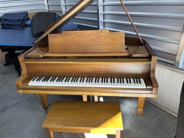 Wooden grand piano in a storage area with a small bench in front