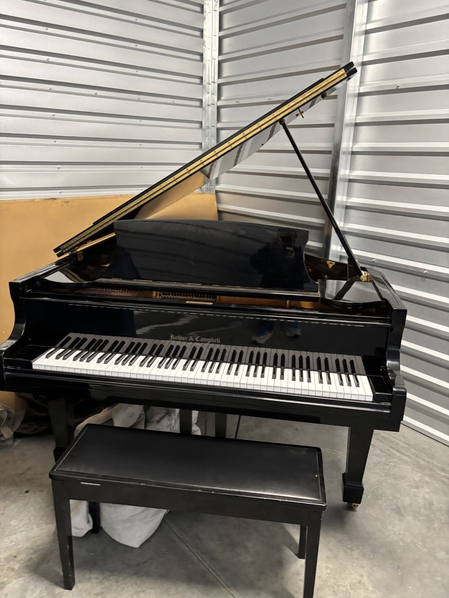 Black grand piano with raised lid and bench in a garage-like room