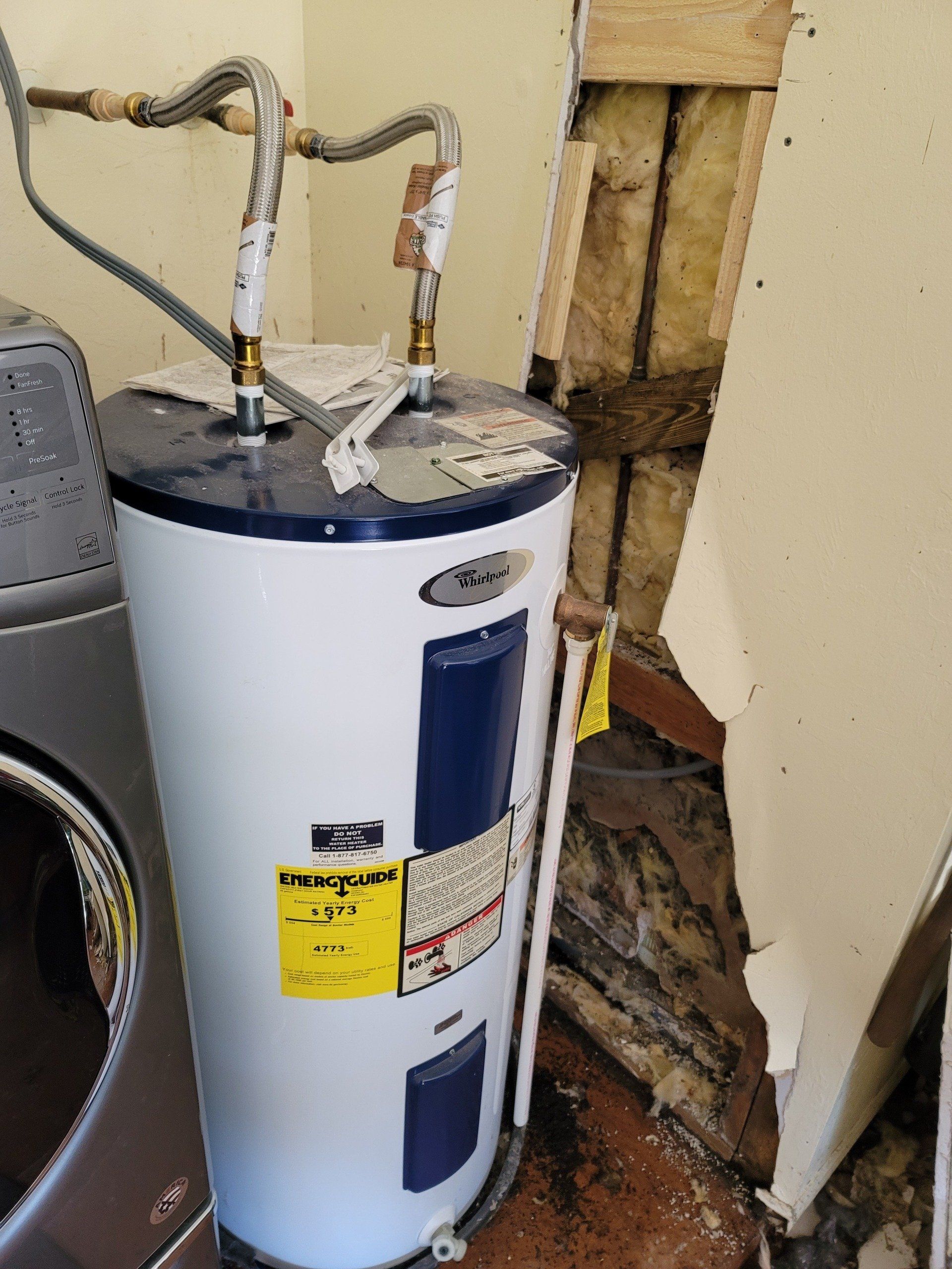 A white water heater is sitting next to a washing machine in a room.