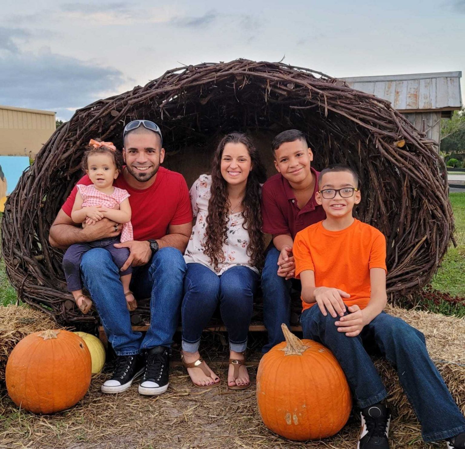 A family is posing for a picture while sitting in a nest surrounded by pumpkins.