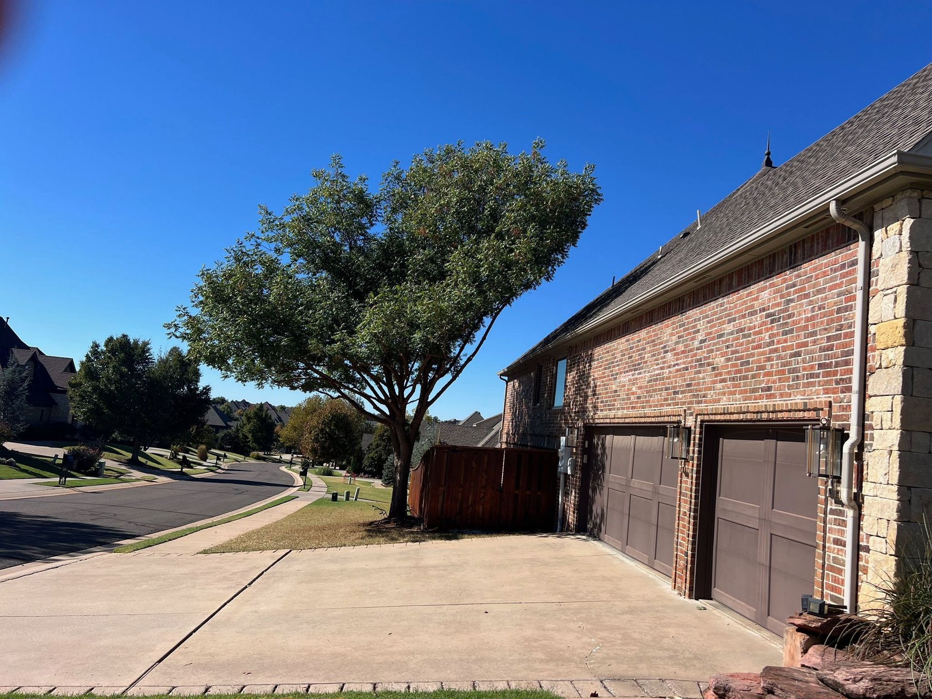 A brick house with two garage doors and a tree in front of it