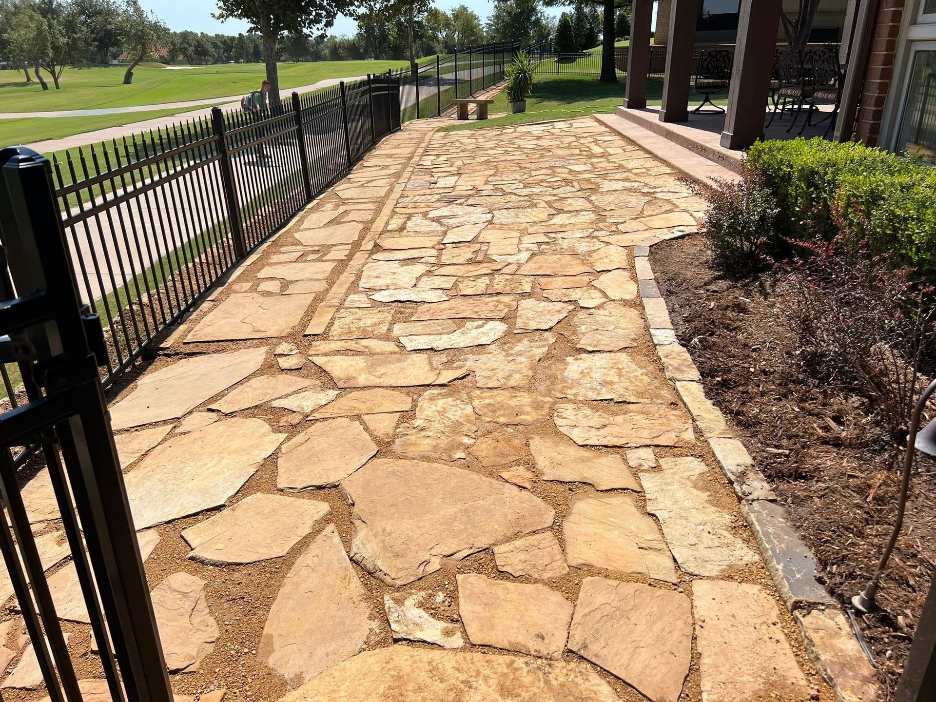 A stone walkway leading to a house with a fence in the background.