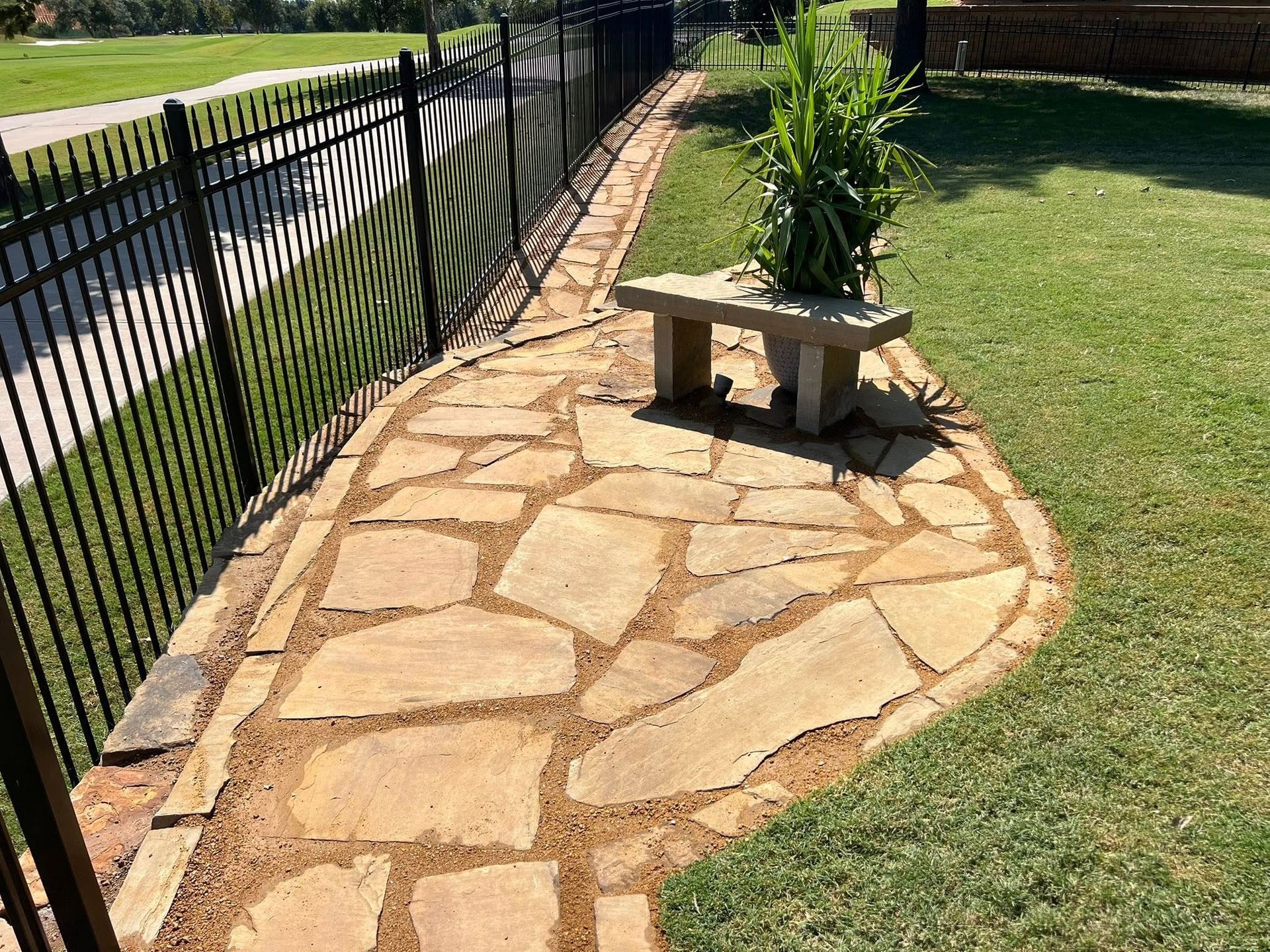 A stone walkway with a bench and a fence in the background.