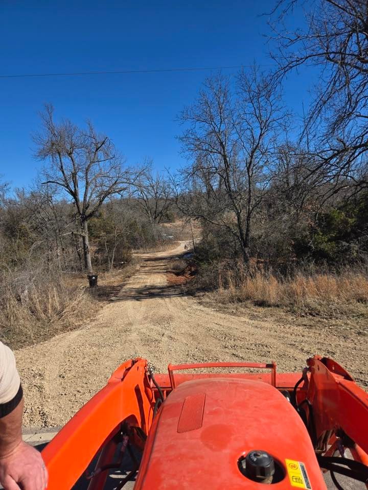 A man is driving an orange tractor down a dirt road.