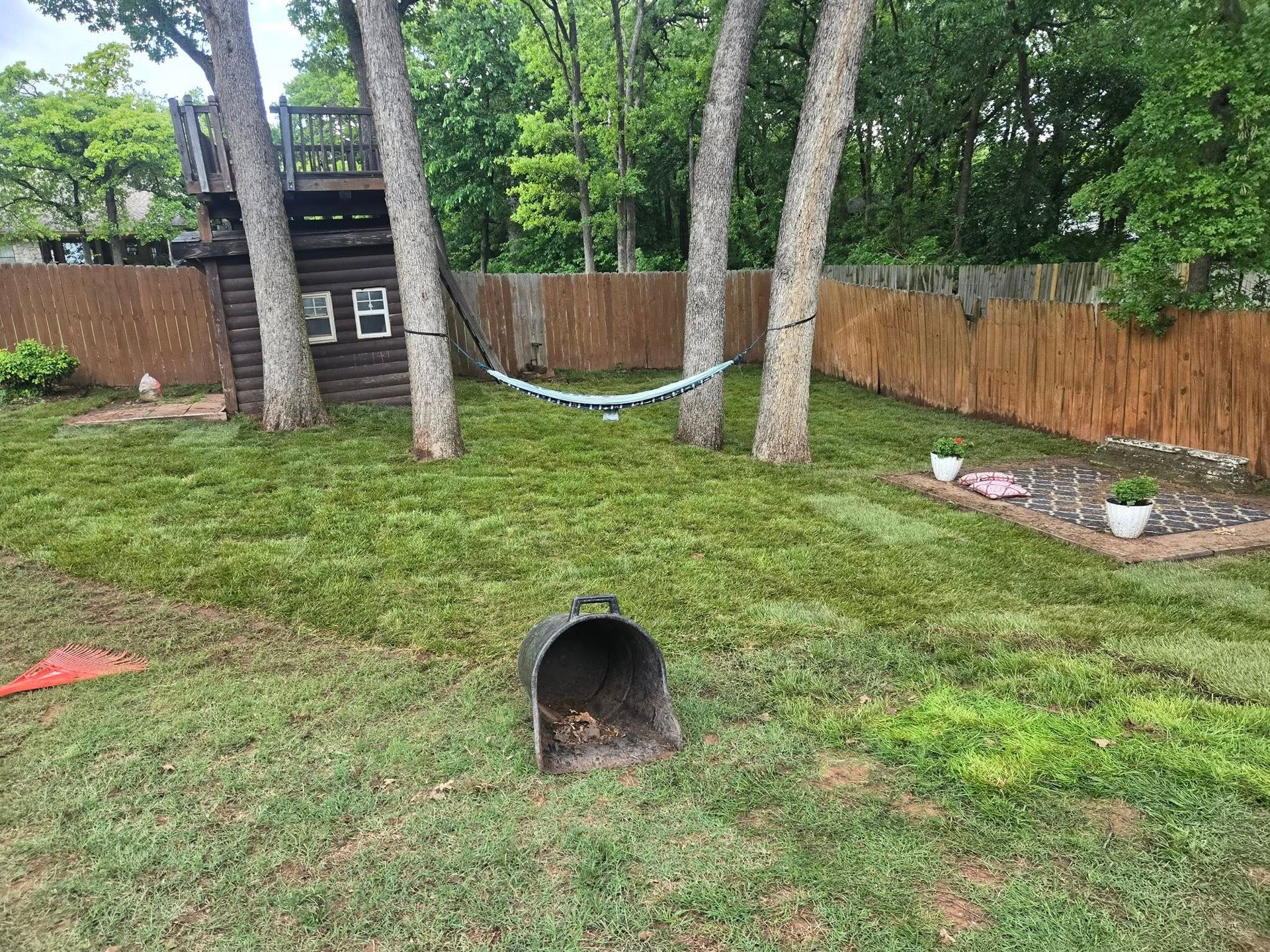 A backyard with a hammock hanging between two trees and a mailbox.