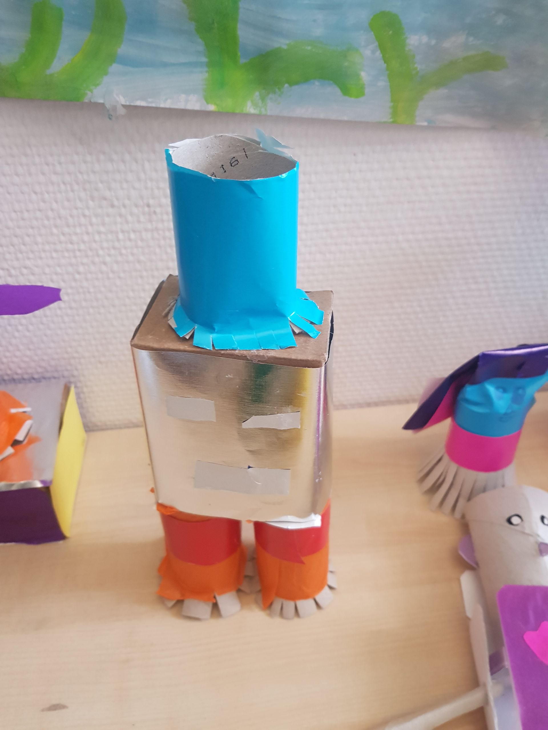 Een robot gemaakt van wc-papierrollen zit op een houten tafel