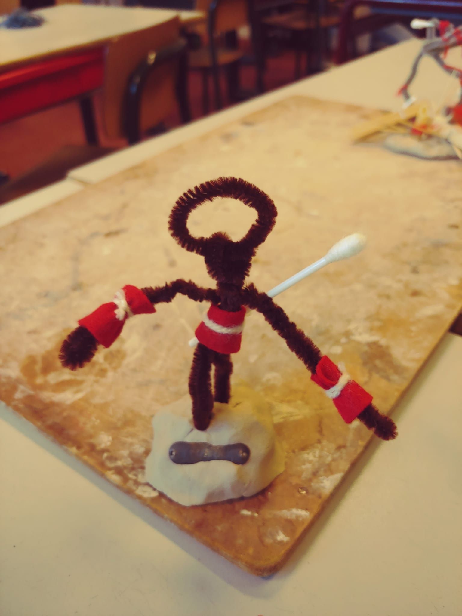 Een figuur  van chenilledraad zit op een tafel