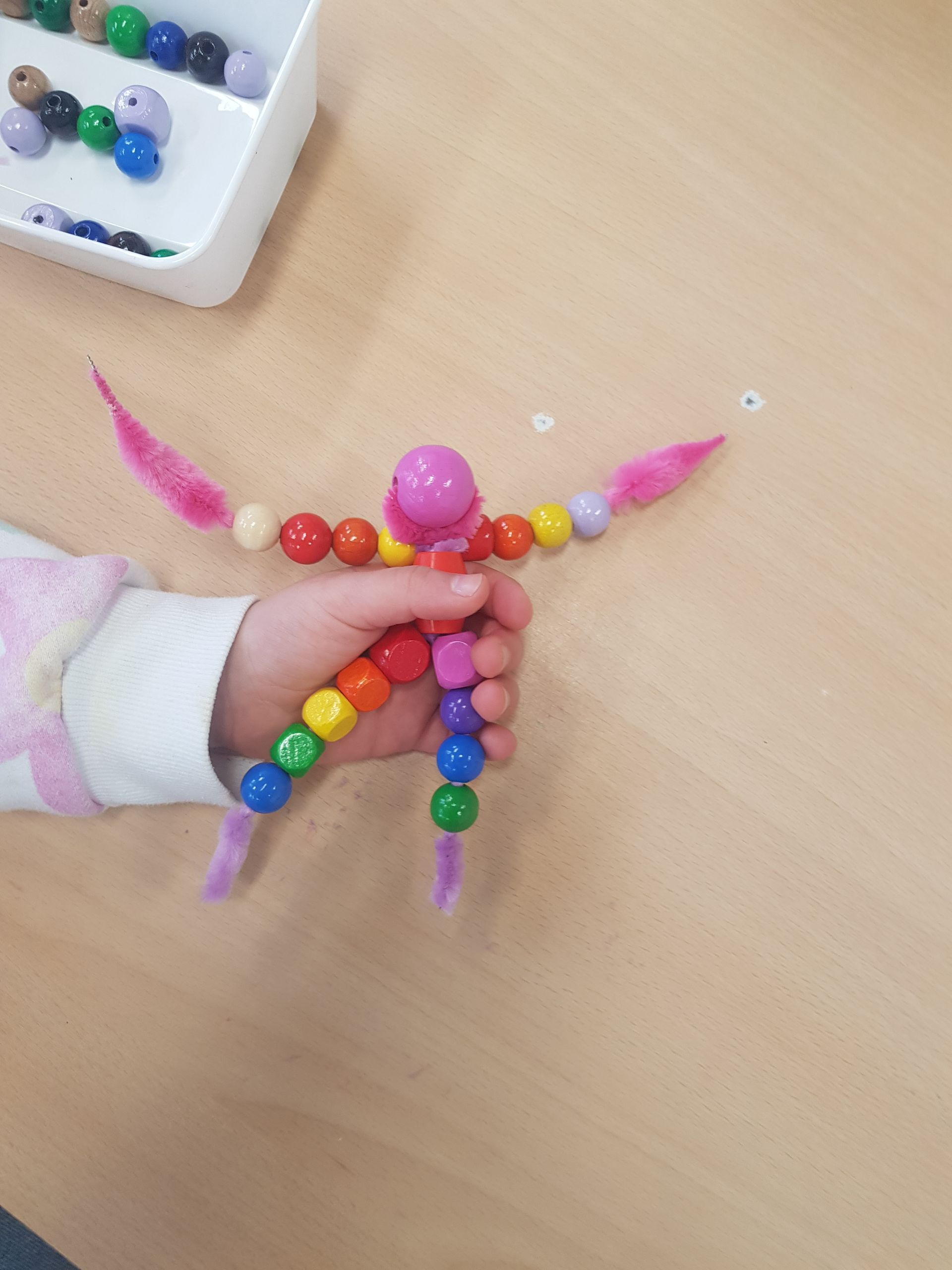 Een kind houdt een speeltje vast dat gemaakt is van kralen en pijpenragers