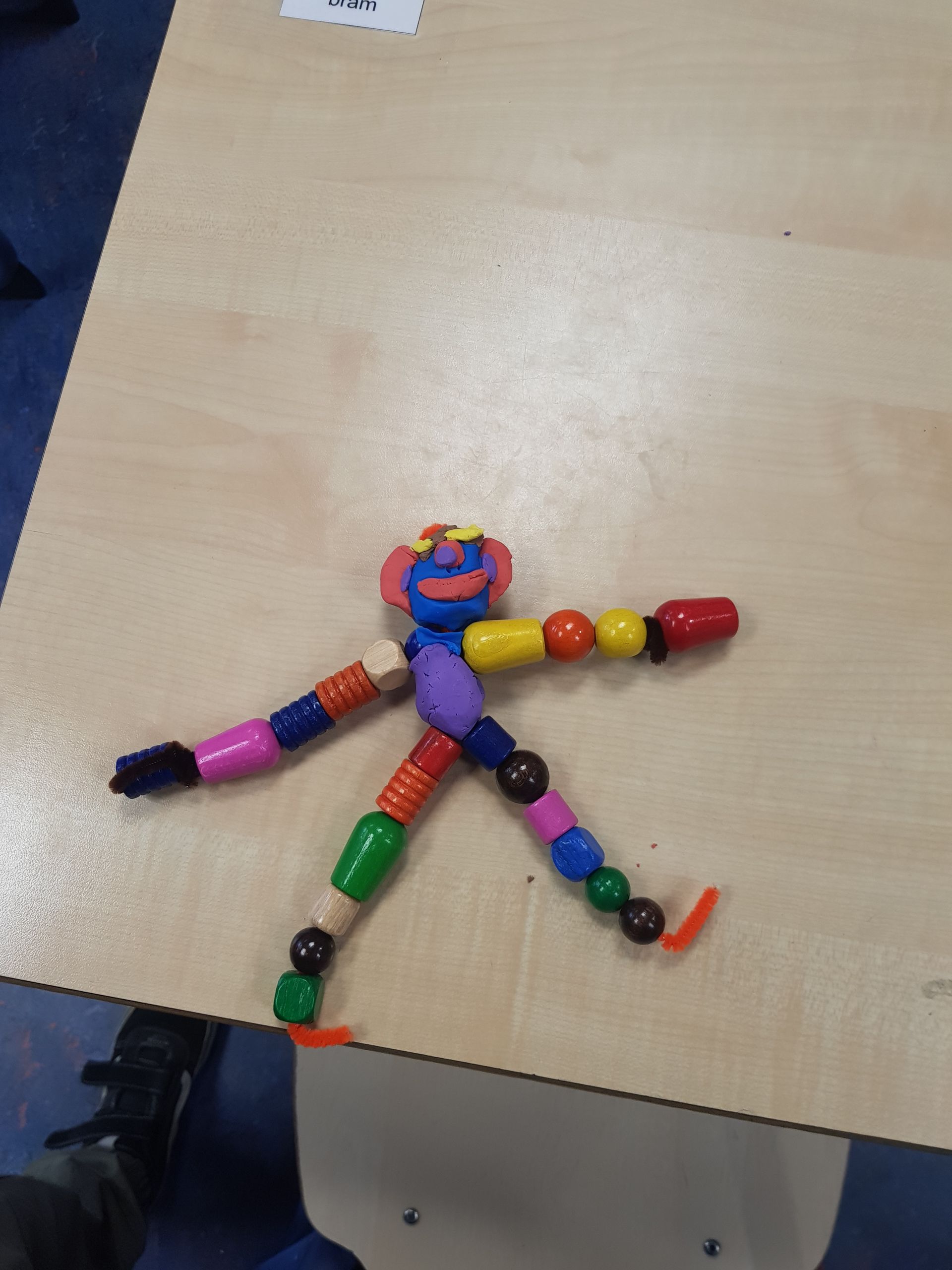 Een poppetje gemaakt van kralen zit op een tafel