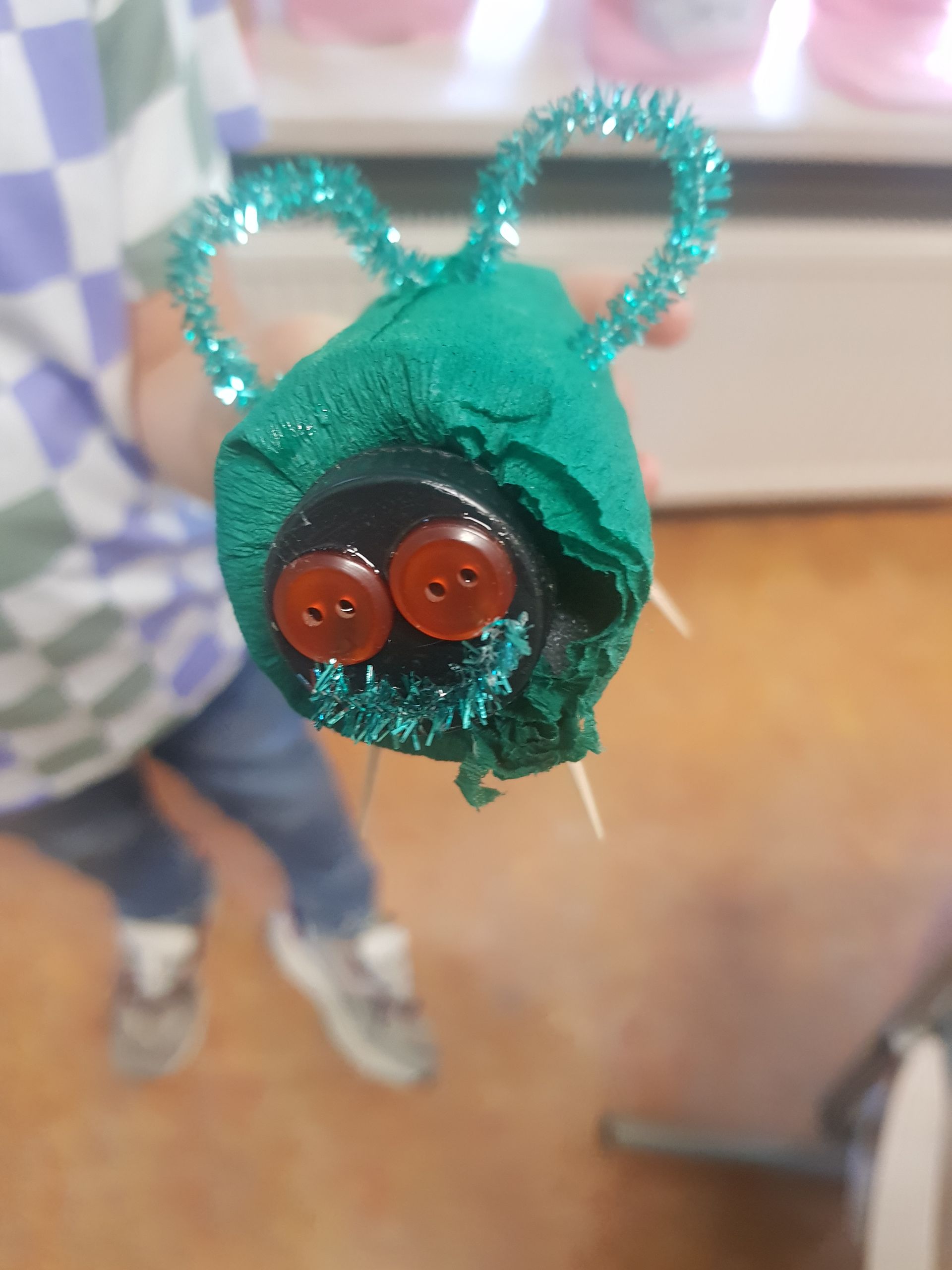 Een kind houdt een groene insect vast die gemaakt is van knopen en pijpenragers
