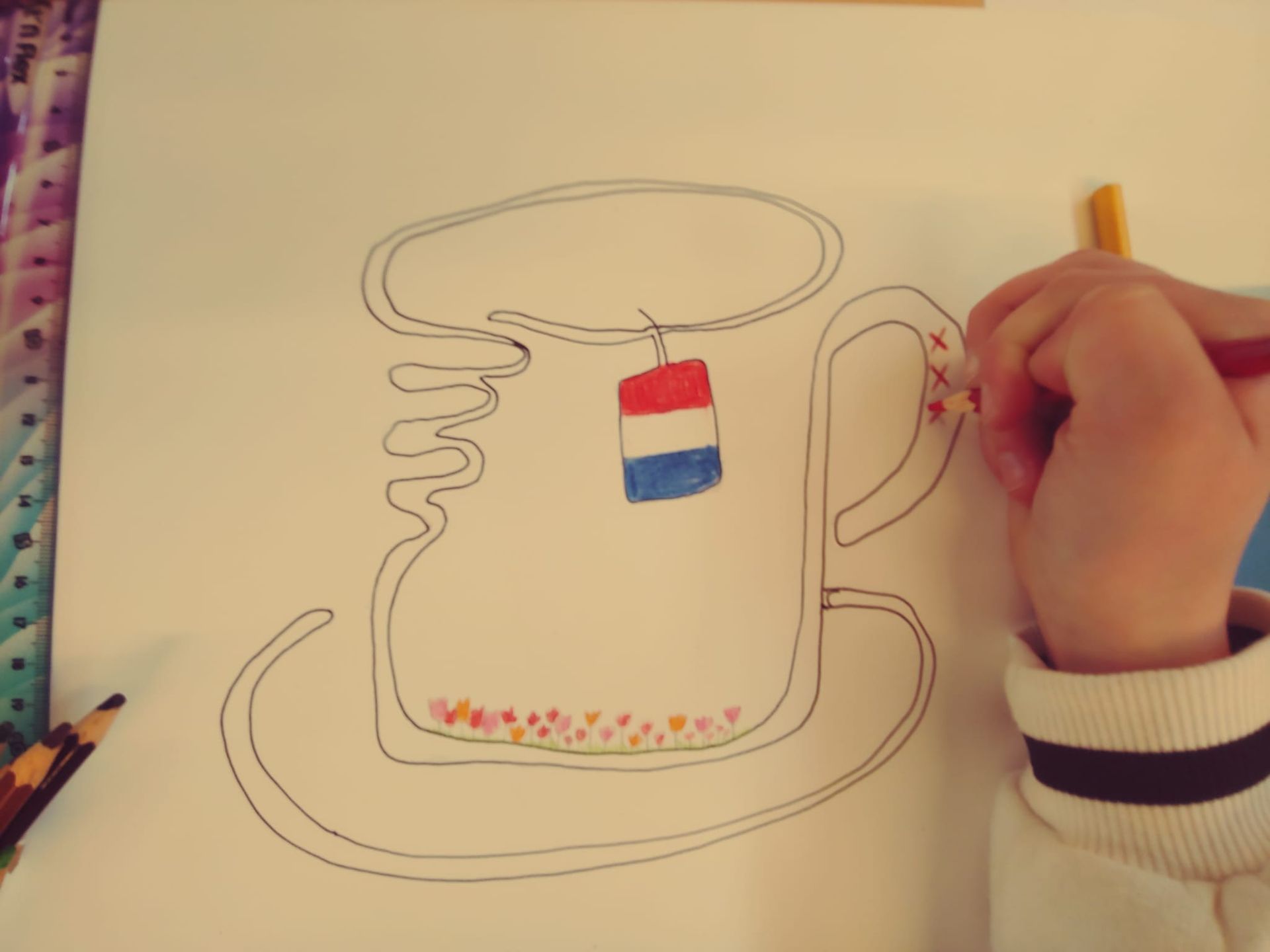 Een kind tekent een kopje thee met een rood wit en blauw theezakje
