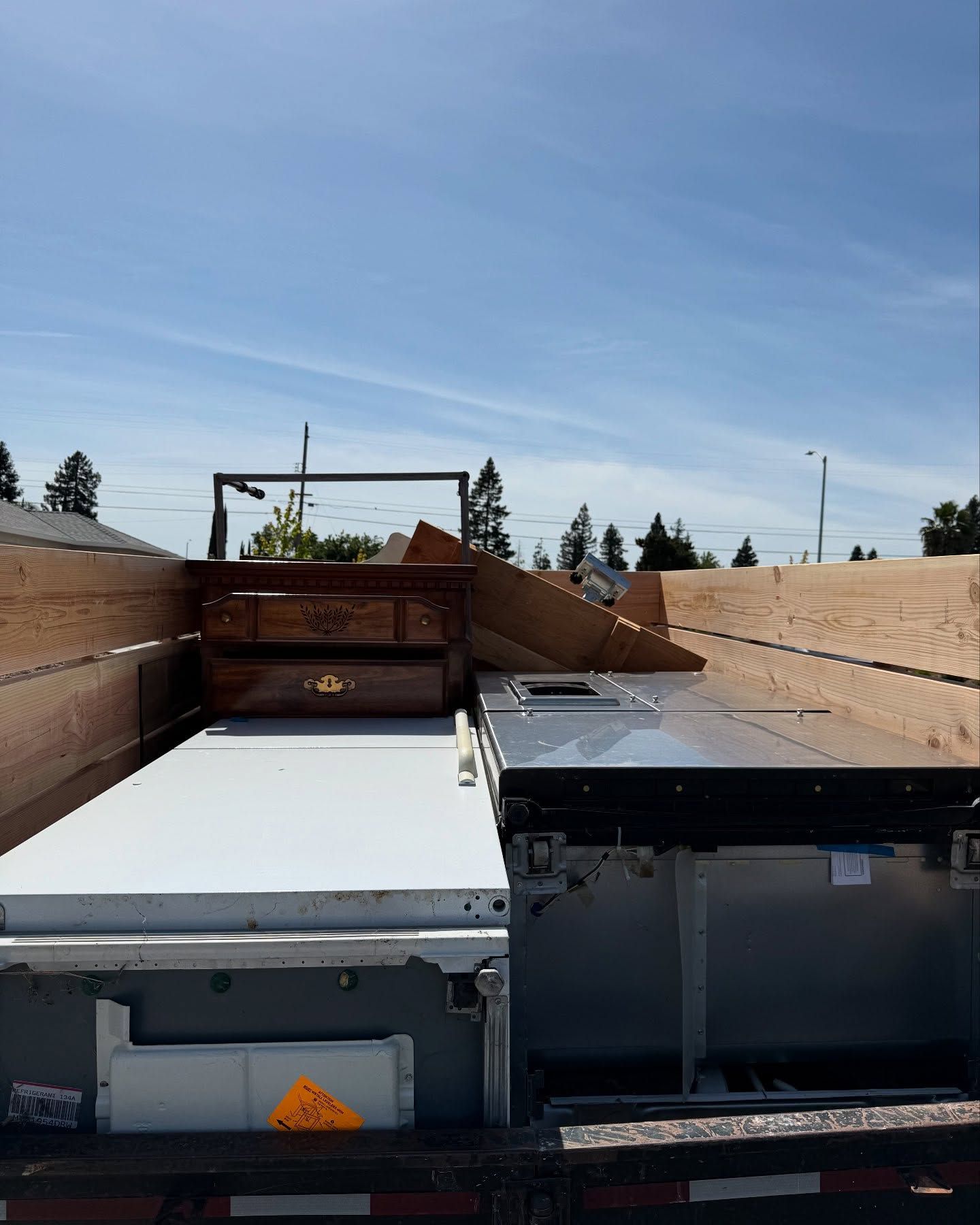 Truck bed with white appliance door, dark appliance, and wood debris under a blue sky.