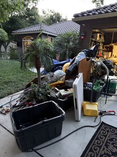 Backyard scene with piled debris, tubs, and a folding table near a house and garage.