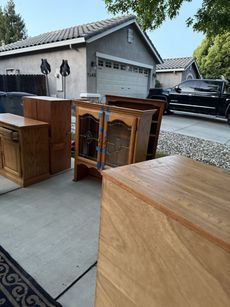 Furniture set out on a driveway, including a cabinet, hutch, and bookshelf. A house and a black truck are in the background.