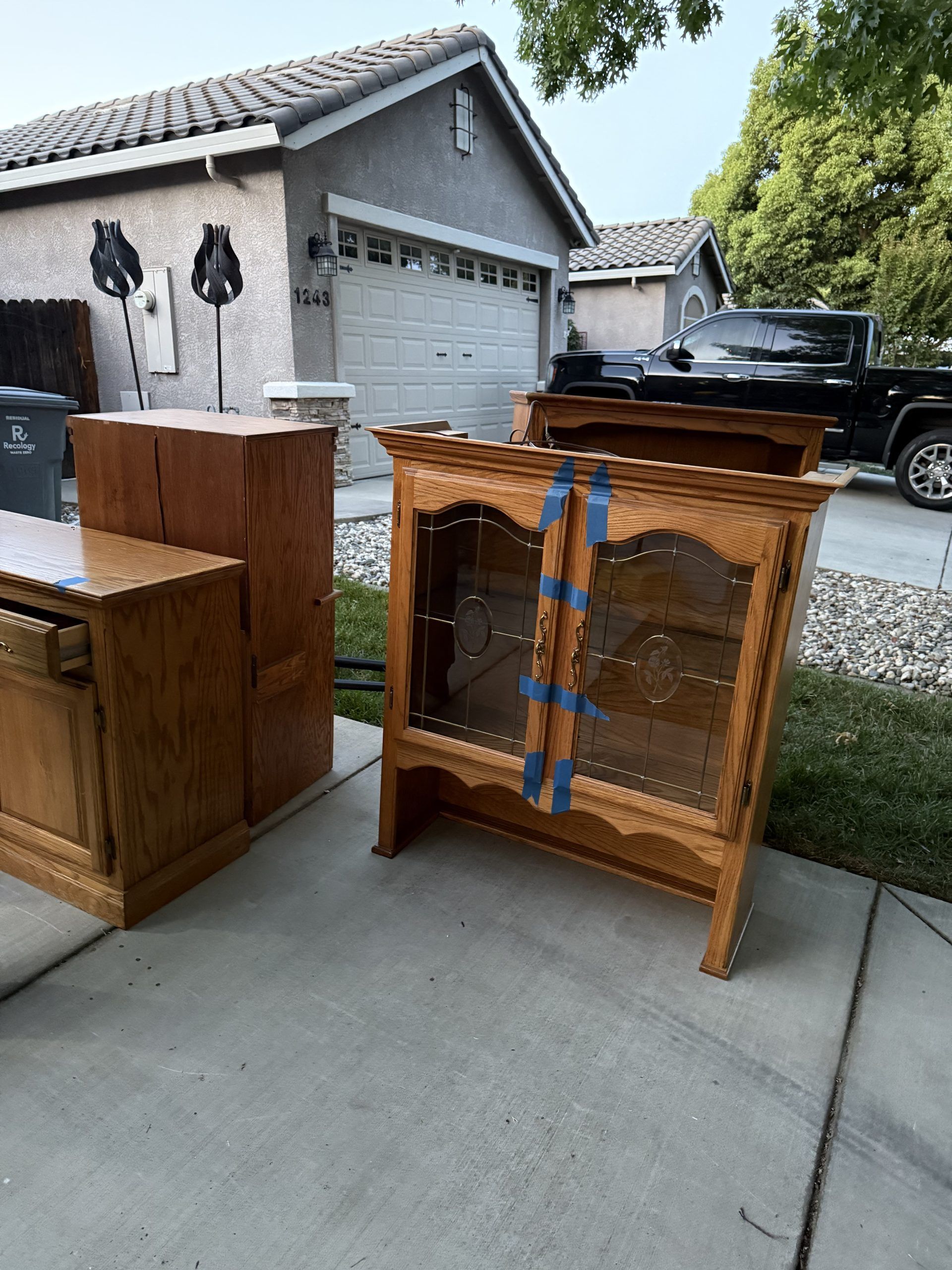 Wooden furniture, including a cabinet, sitting on a driveway in front of a house.
