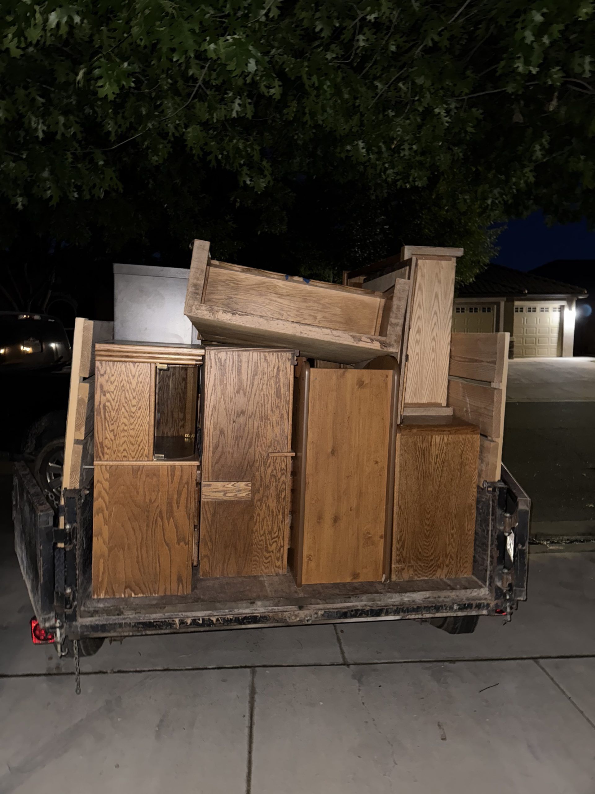 A trailer loaded with various wooden furniture pieces, viewed at night with a dark background.