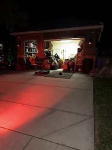 Garage interior filled with items, illuminated by a bright light. Red light from an unknown source on the concrete driveway.