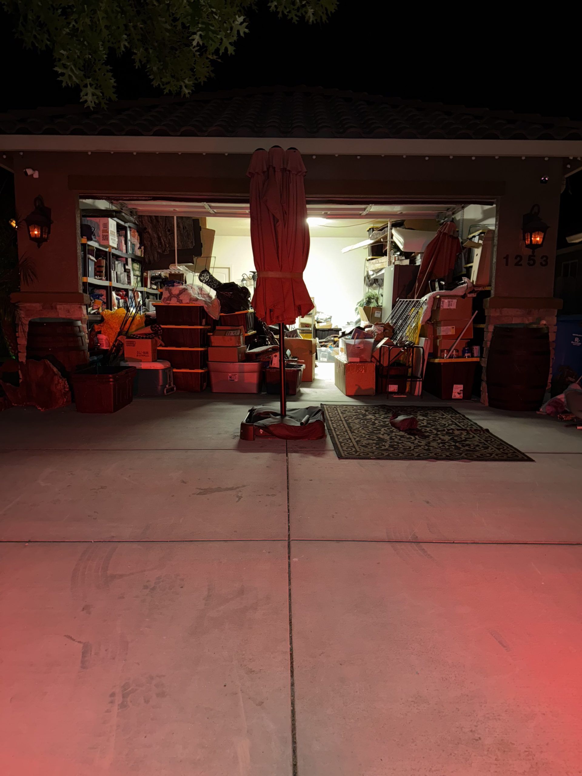 Garage open with items overflowing; an umbrella in the center. Night scene.