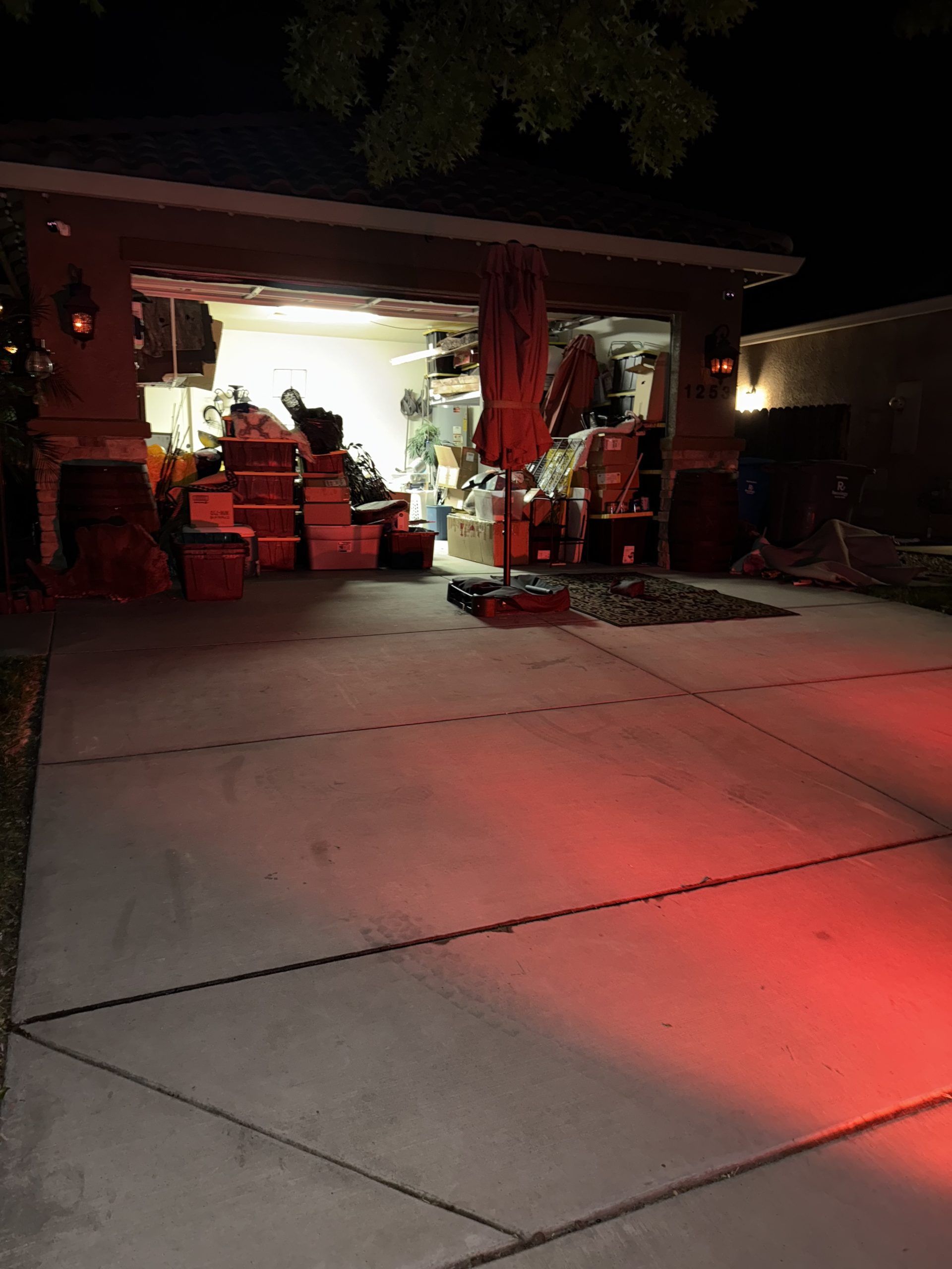 Garage at night with boxes, furniture, and an open door; red light on the ground.