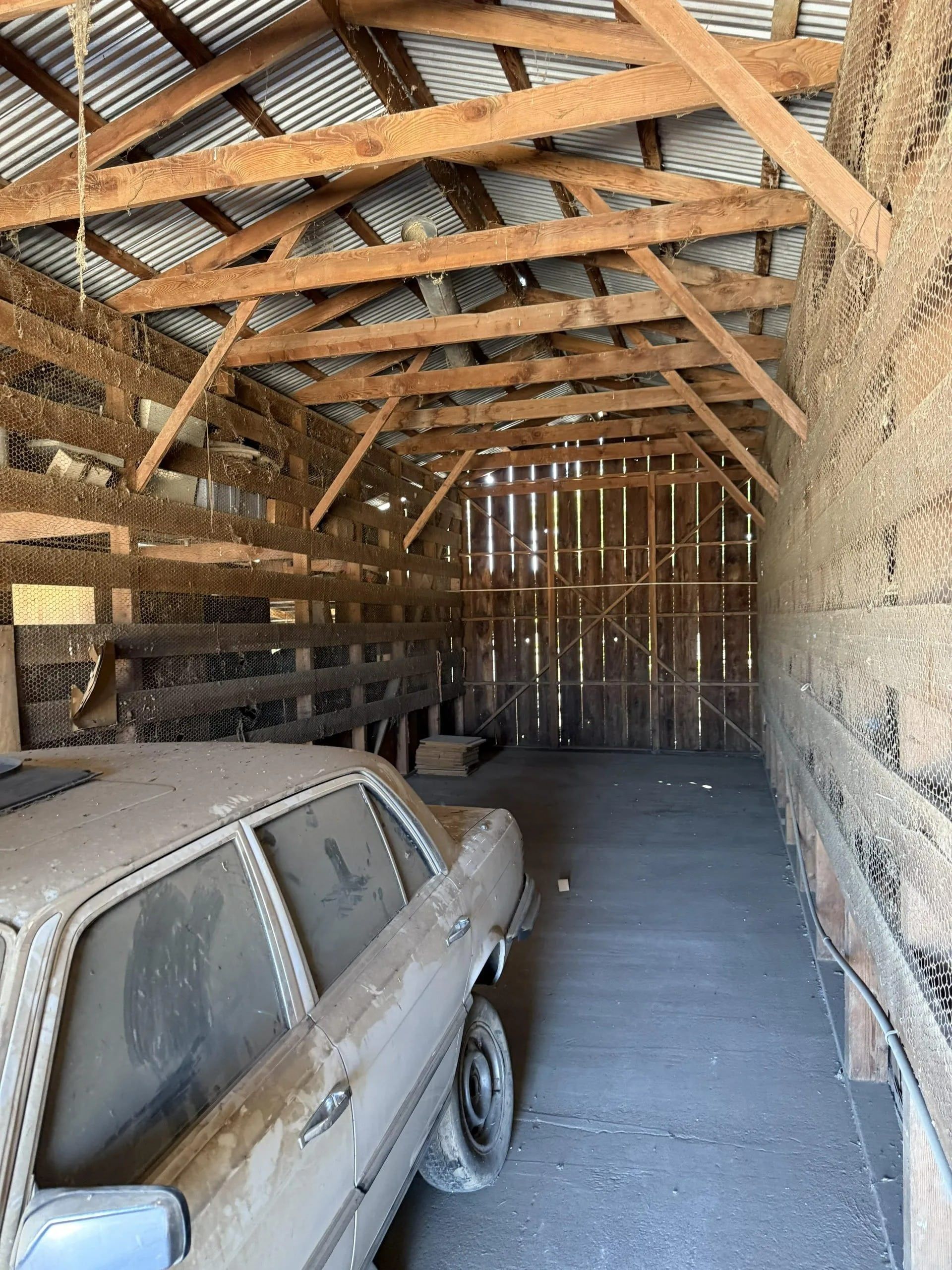 Dusty abandoned barn interior with old car parked inside.