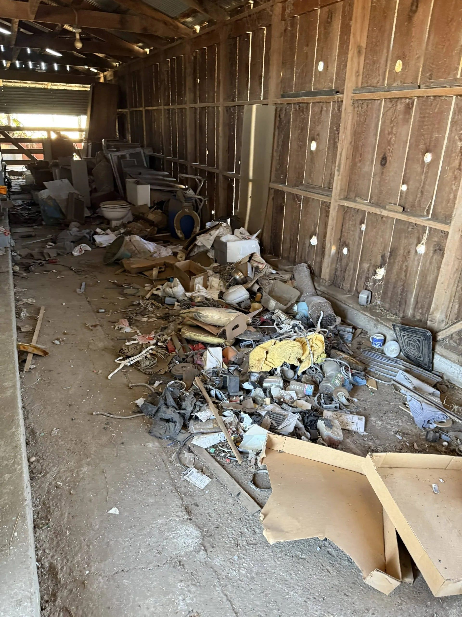 Messy interior of a wooden shed. Piles of trash and debris cover the floor.
