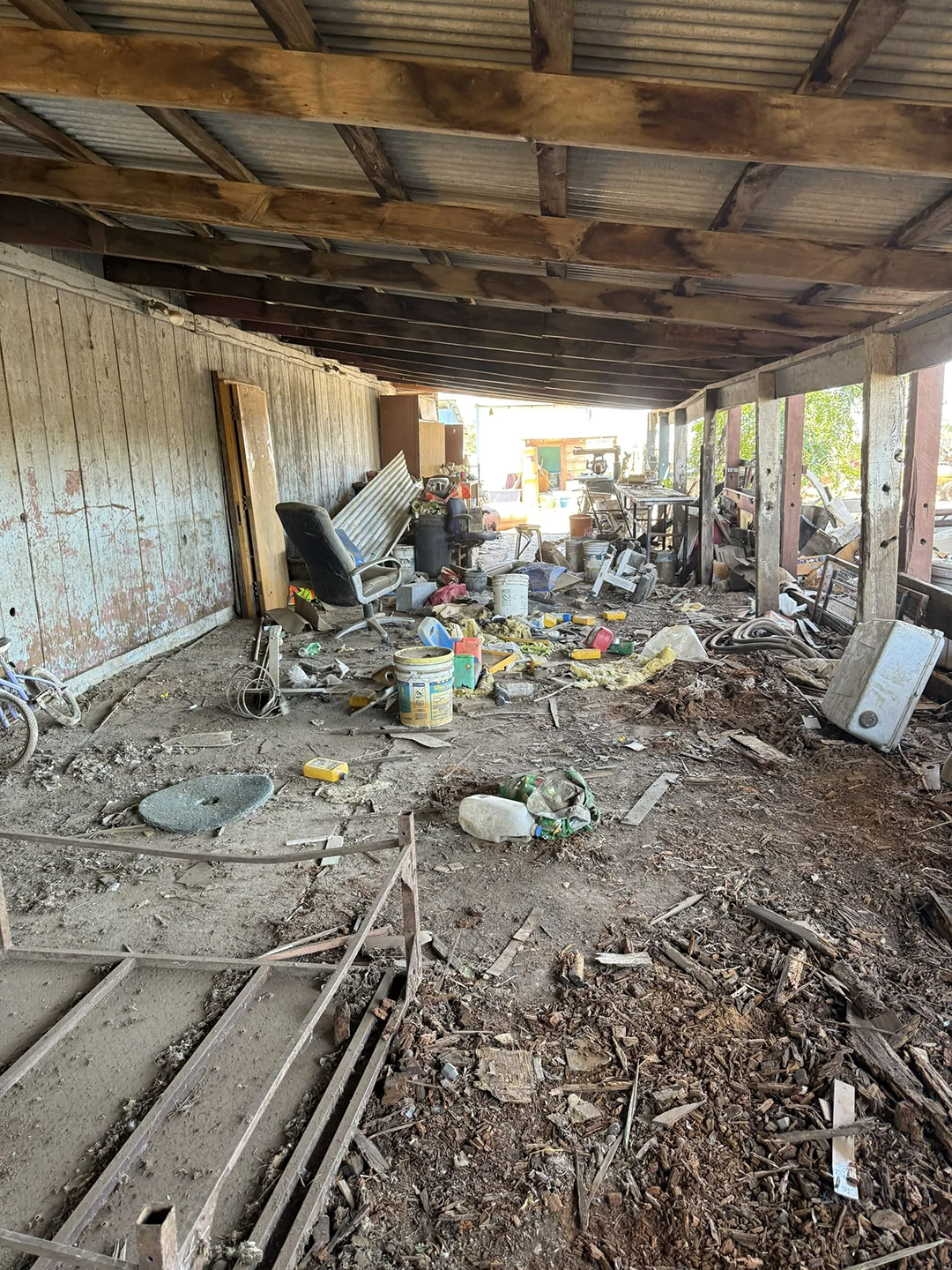 Messy, cluttered open-air storage area; debris, trash, and various objects litter the ground.