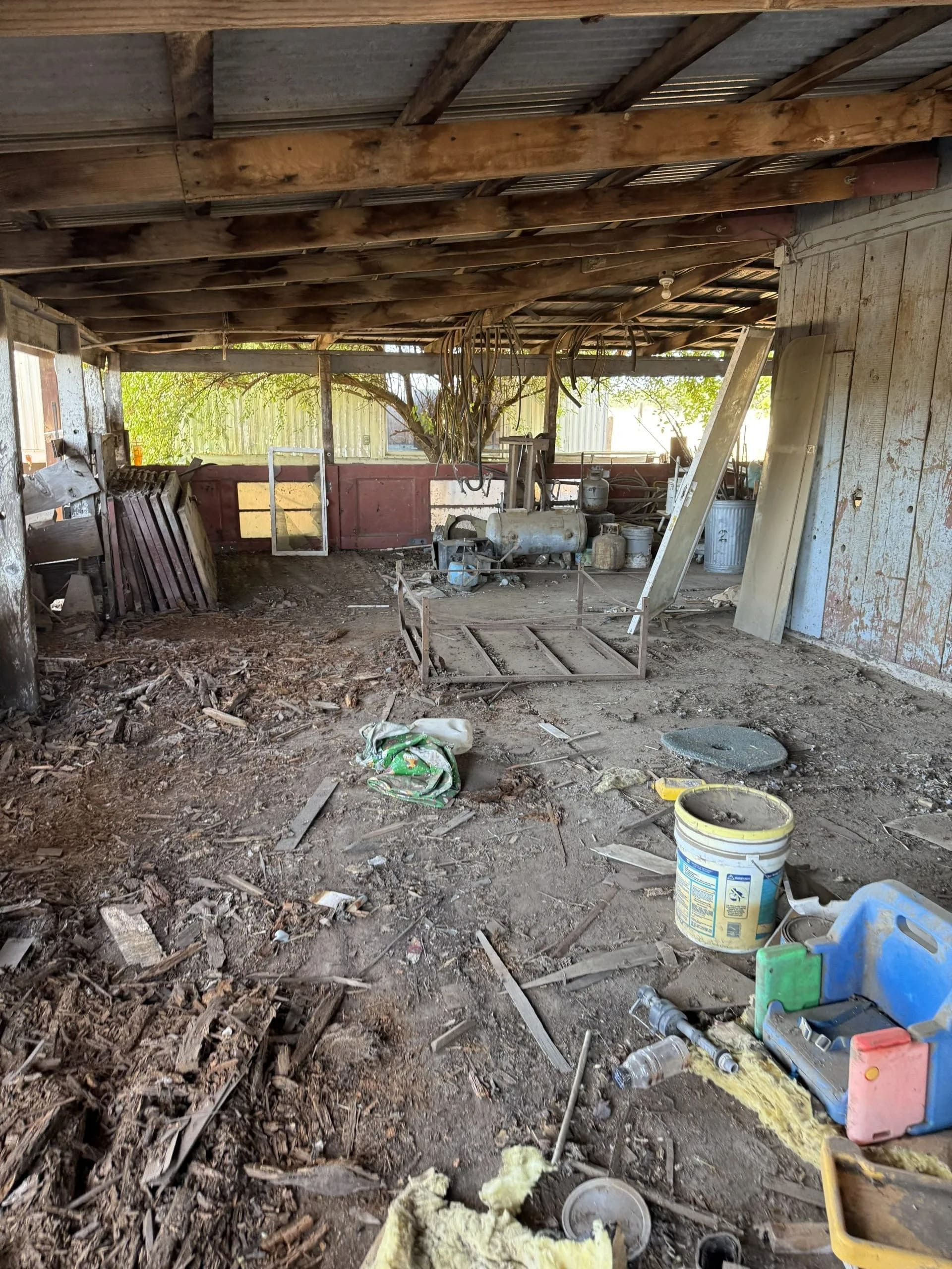 Interior of a dilapidated, open-air barn with debris on the dirt floor.