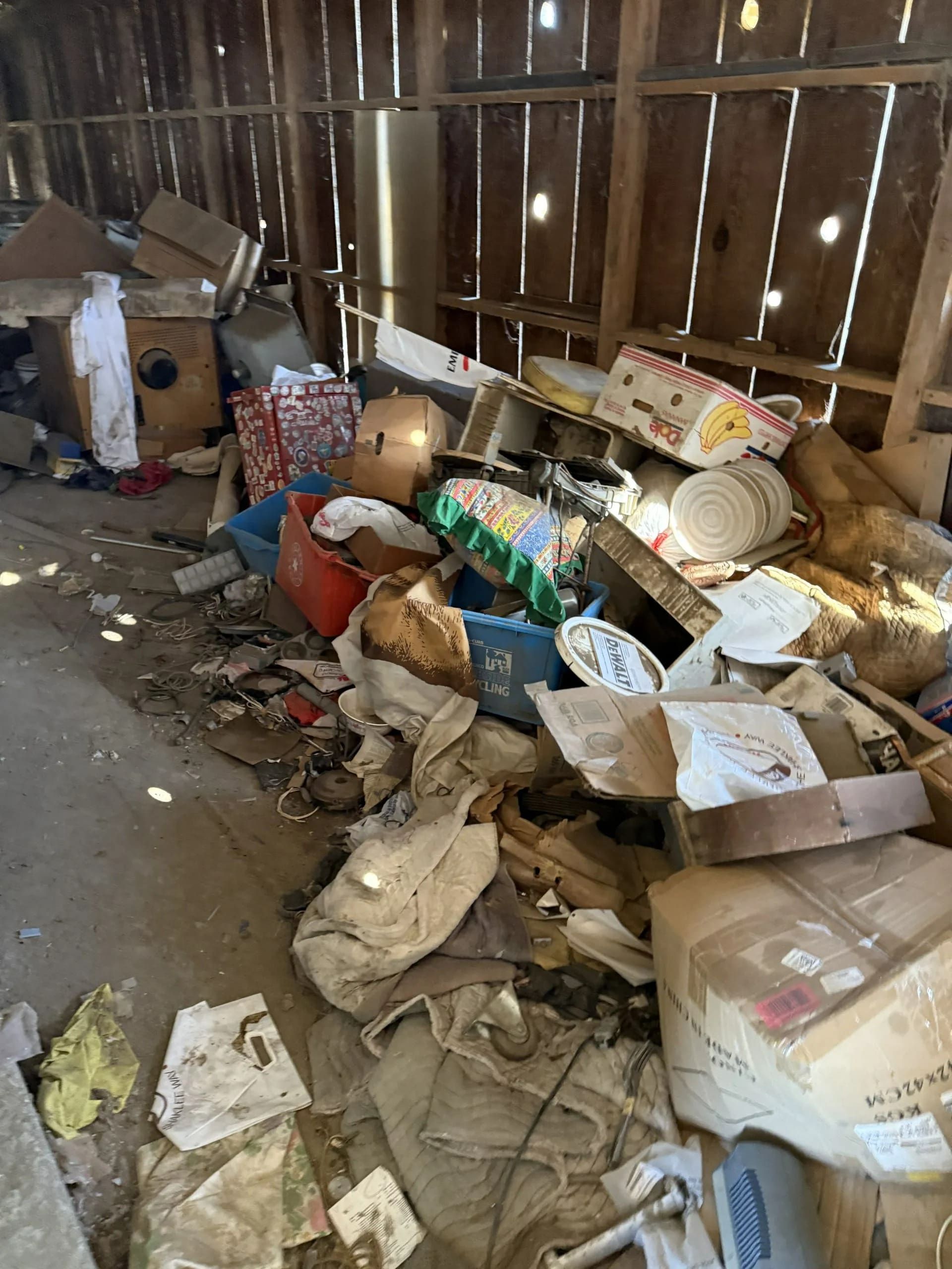 Messy, cluttered storage room; debris and boxes piled against wooden wall.