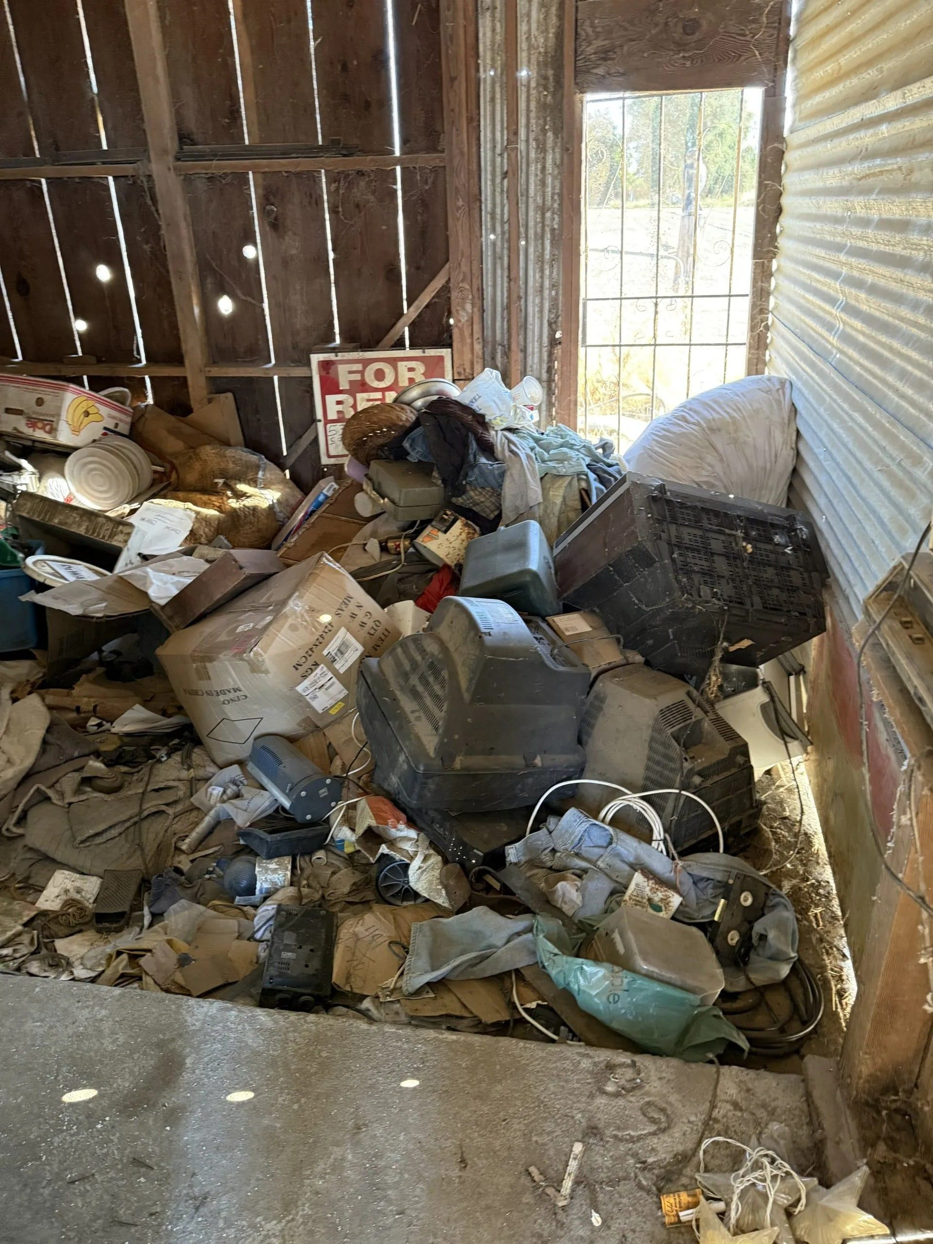 Pile of trash in a barn, including old TVs, with a 