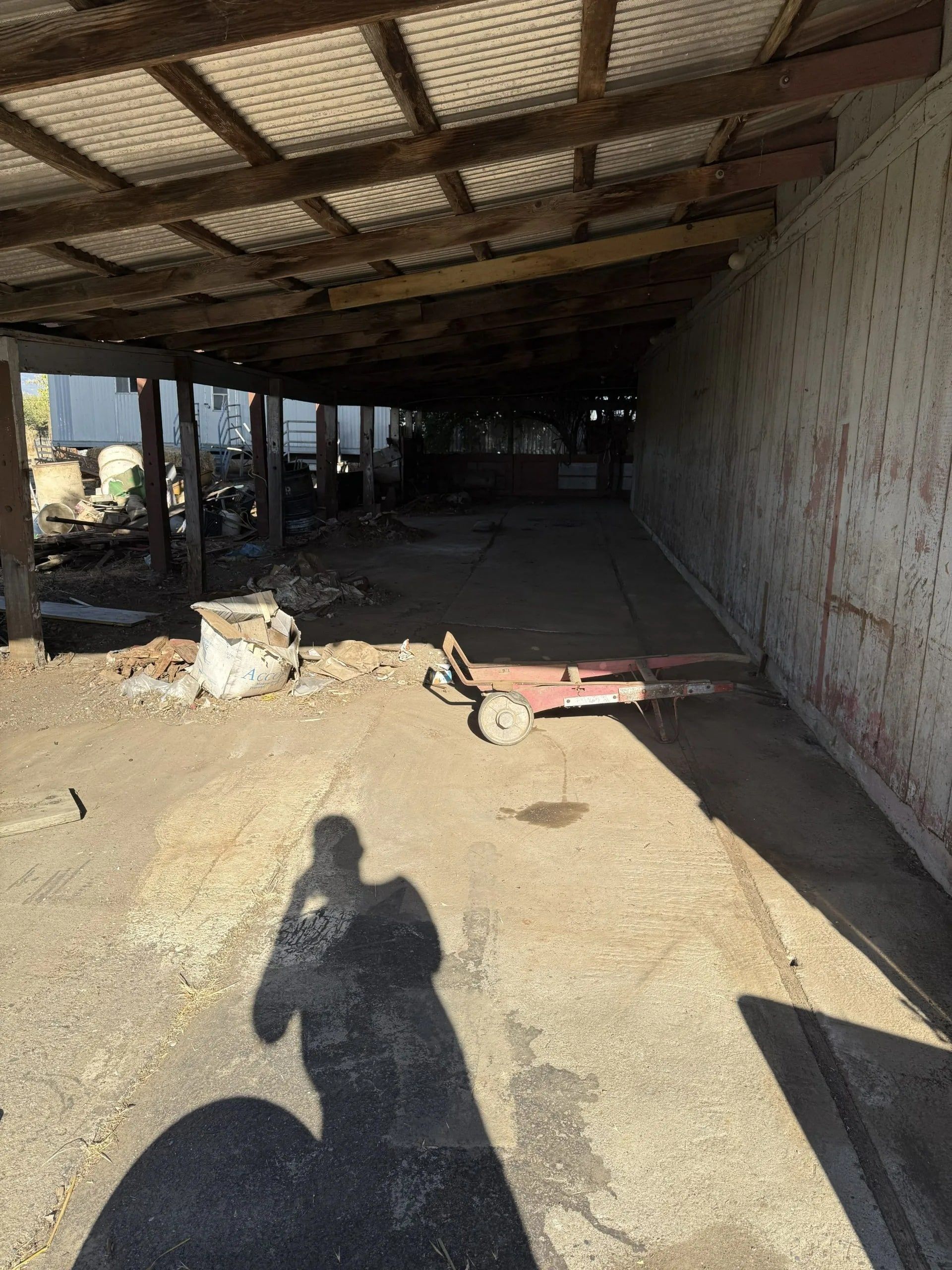 Shadow of a person taking a photo inside a dilapidated, open-air structure. Red cart and debris are visible.