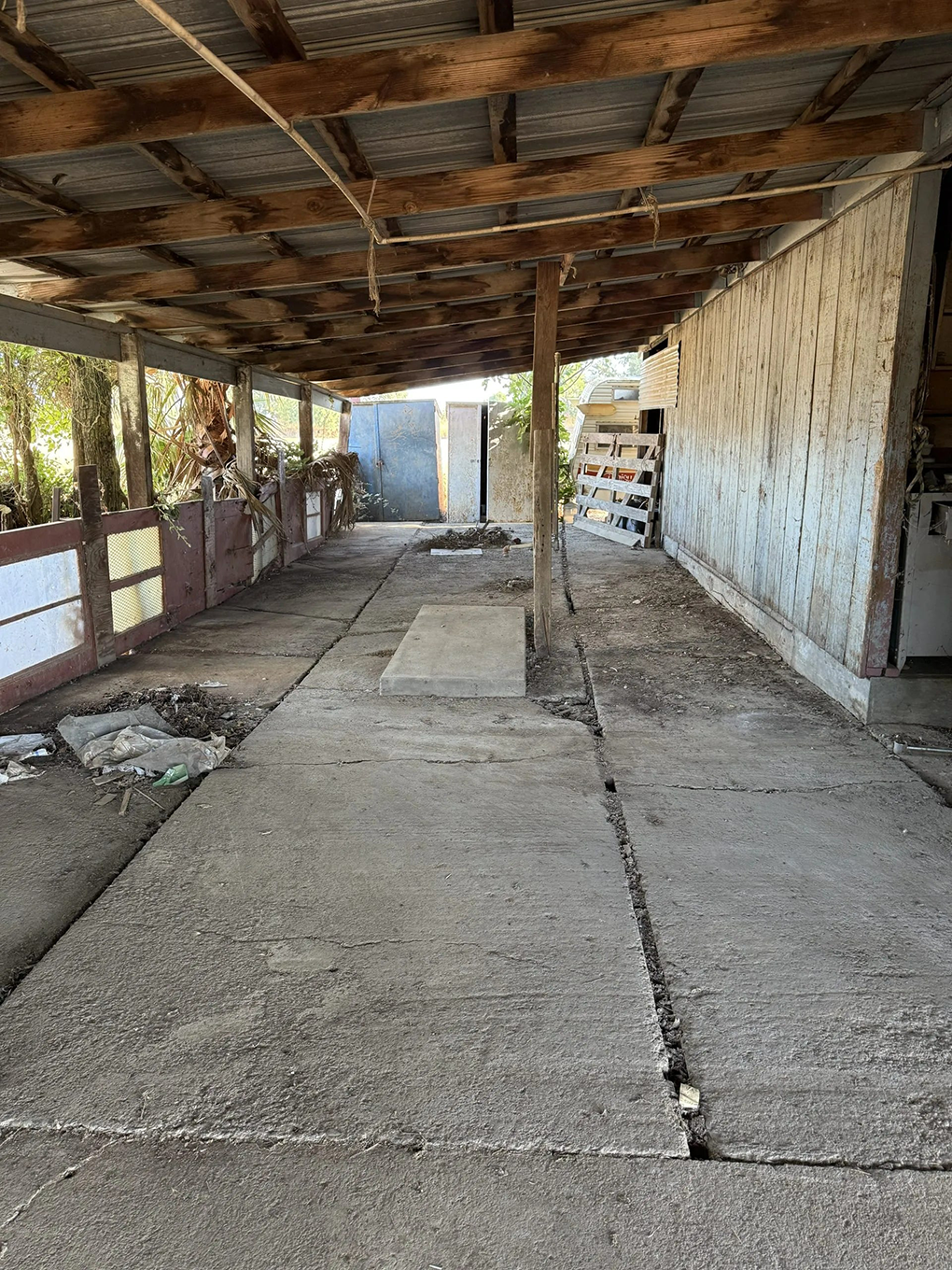 Concrete walkway under a weathered wooden awning; cracked path with a glimpse of a distant door.