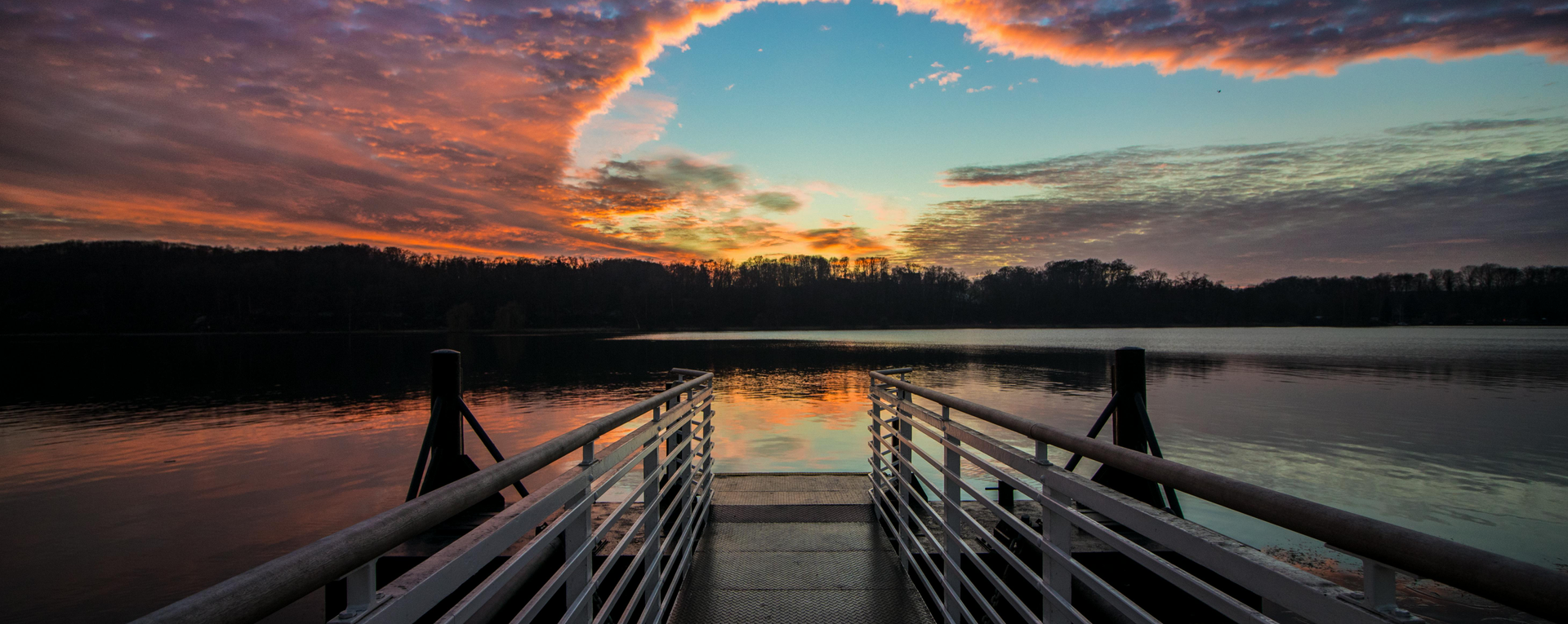 Sunset over a quiet lake with a dock walkway in Delaware