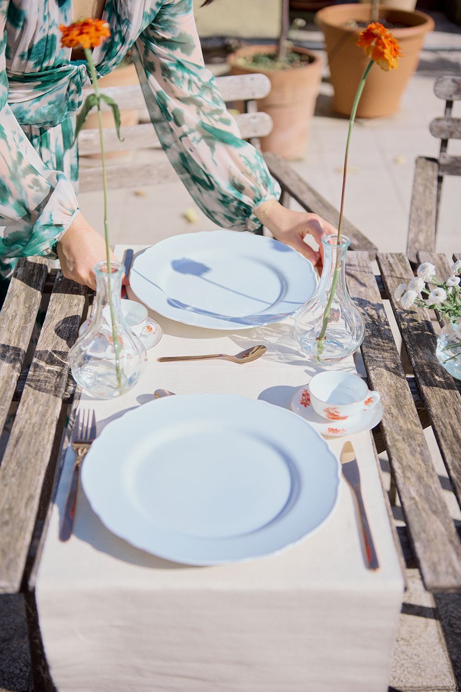 Una donna sta apparecchiando la tavola con piatti, utensili e vasi.