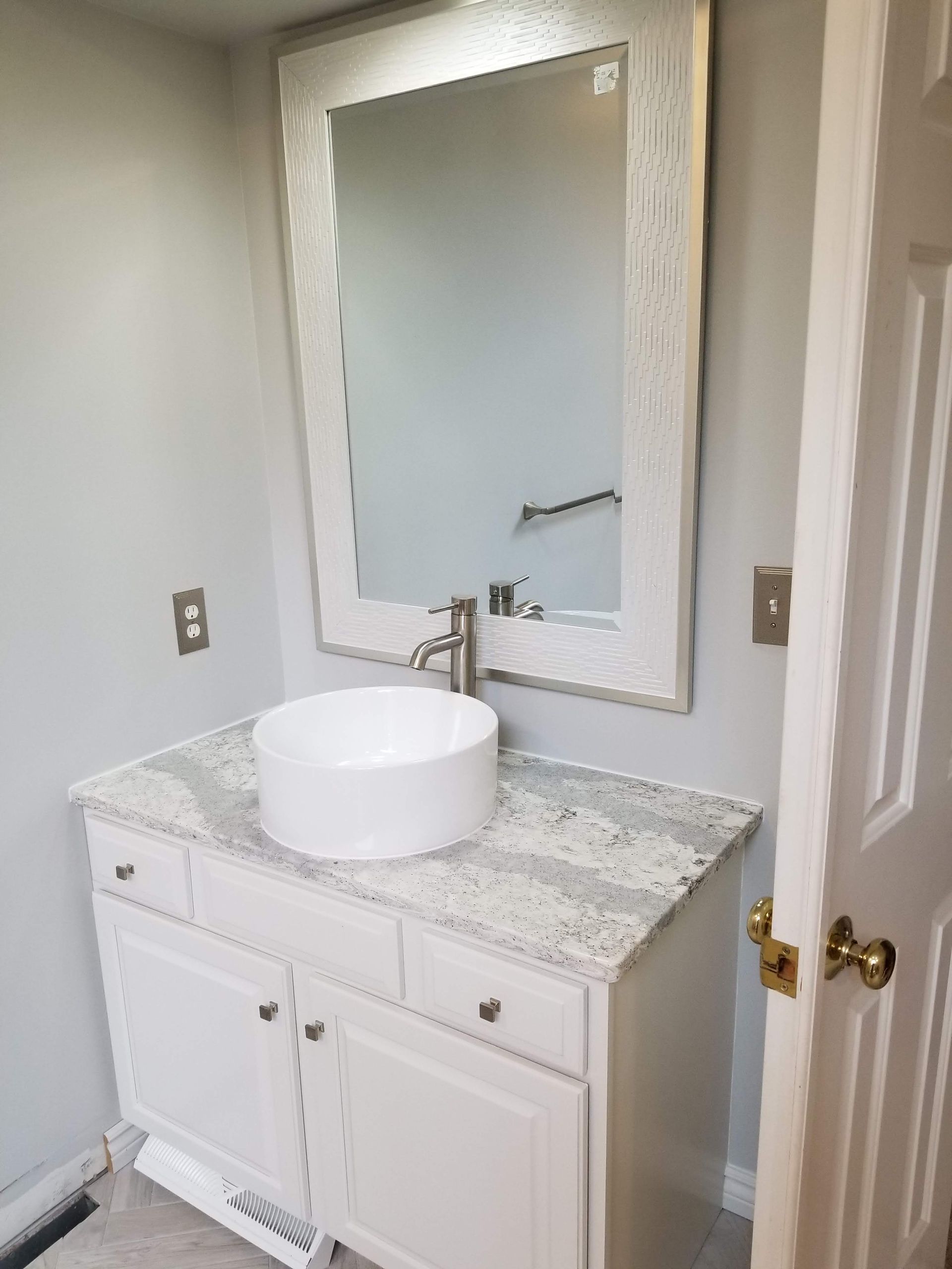 White bathroom vanity with vessel sink and textured mirror frame.