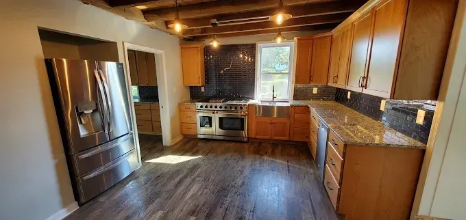 Kitchen with stainless steel appliances, wooden cabinets, and dark tile backsplash.