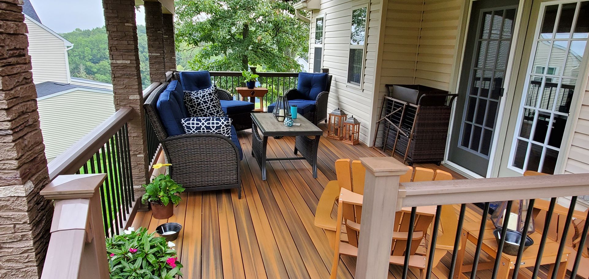 A furnished porch with a wicker sofa, chairs, and table. Wooden deck with a view of greenery.