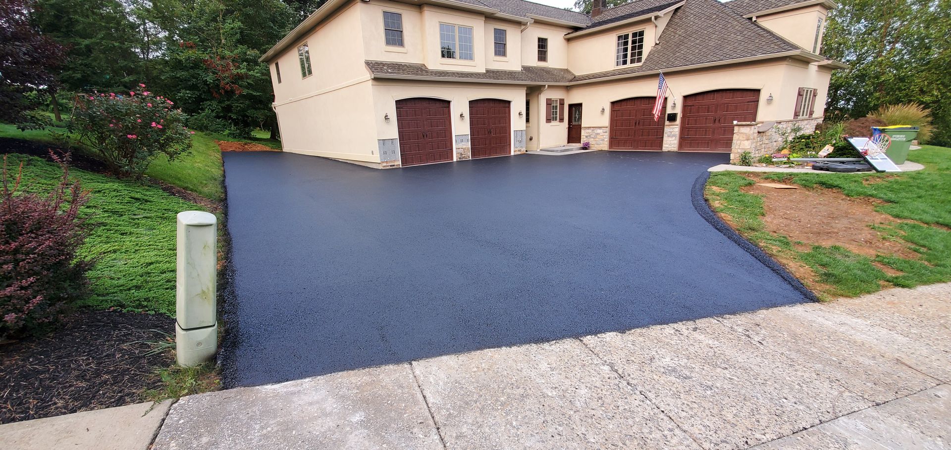 Paved driveway in front of a tan two-story house with dark brown garage doors.