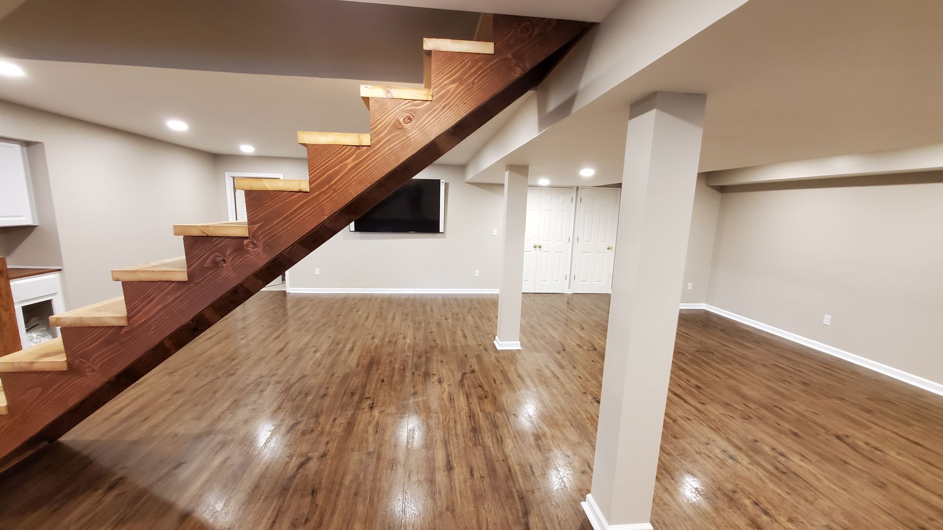 Finished basement with wood flooring, stairs, and support beams.