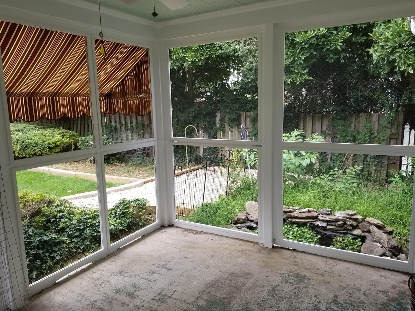 Screened-in porch with concrete floor and white frames, looking out onto a backyard with greenery and a small pond.