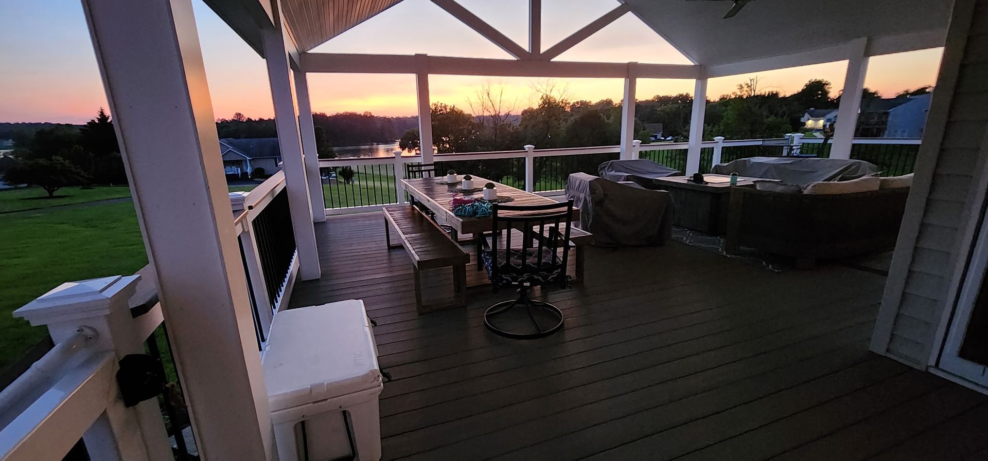 Covered porch with dining table set for a meal, overlooking a lake at sunset.
