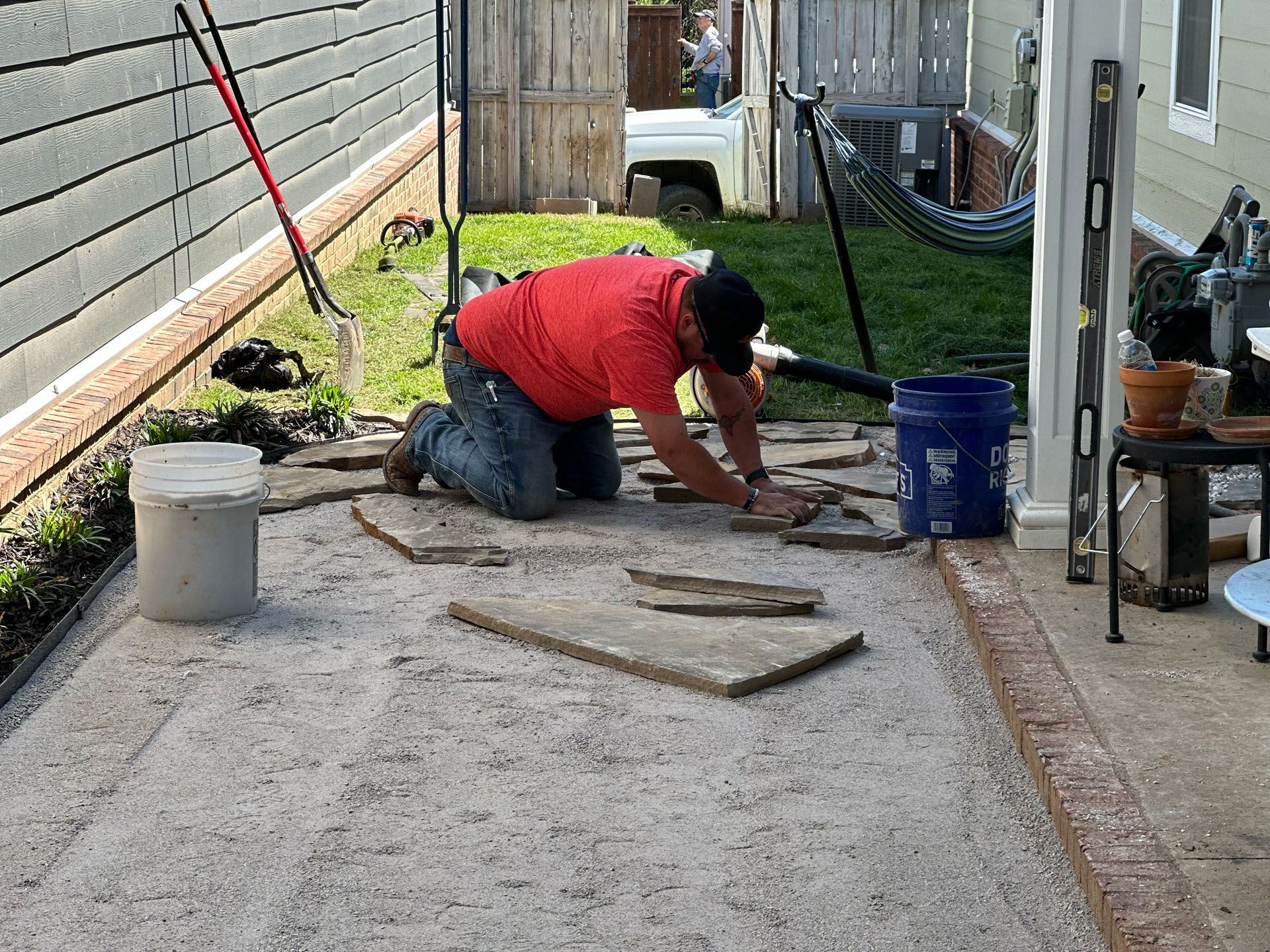 A man is kneeling down on the ground working on a patio.