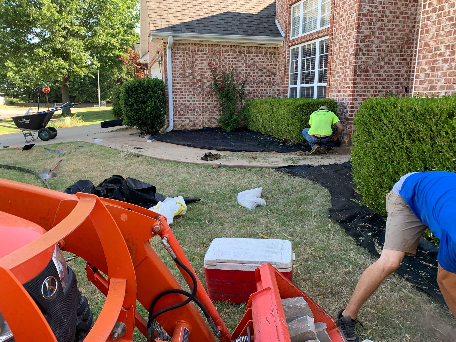 Two men are working on a lawn in front of a brick house.
