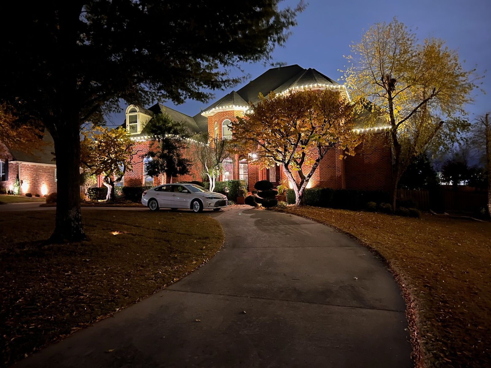 A white car is parked in front of a brick house at night.