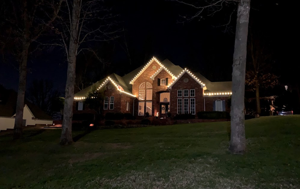 A large house with christmas lights on it is lit up at night.