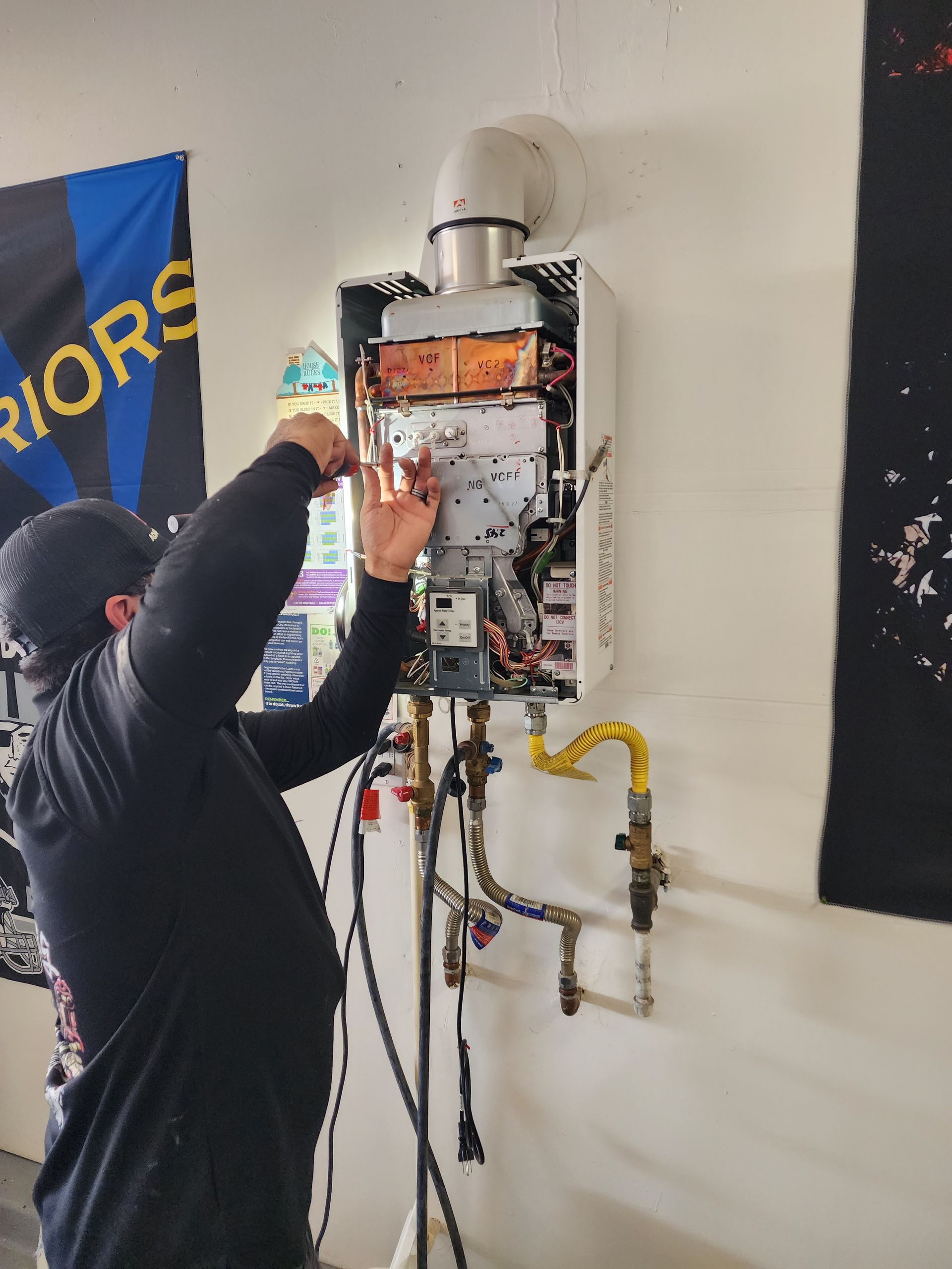 A man is working on a water heater in front of a banner that says warriors