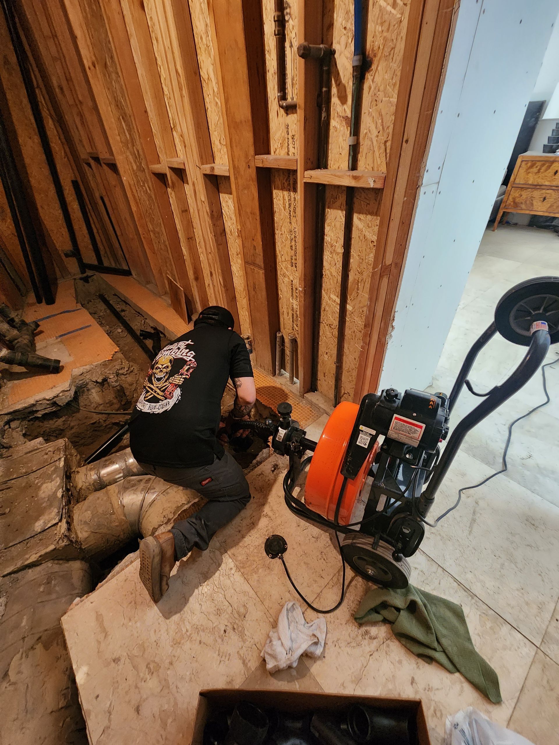 A man in a black shirt with a skull on the back is working on a pipe