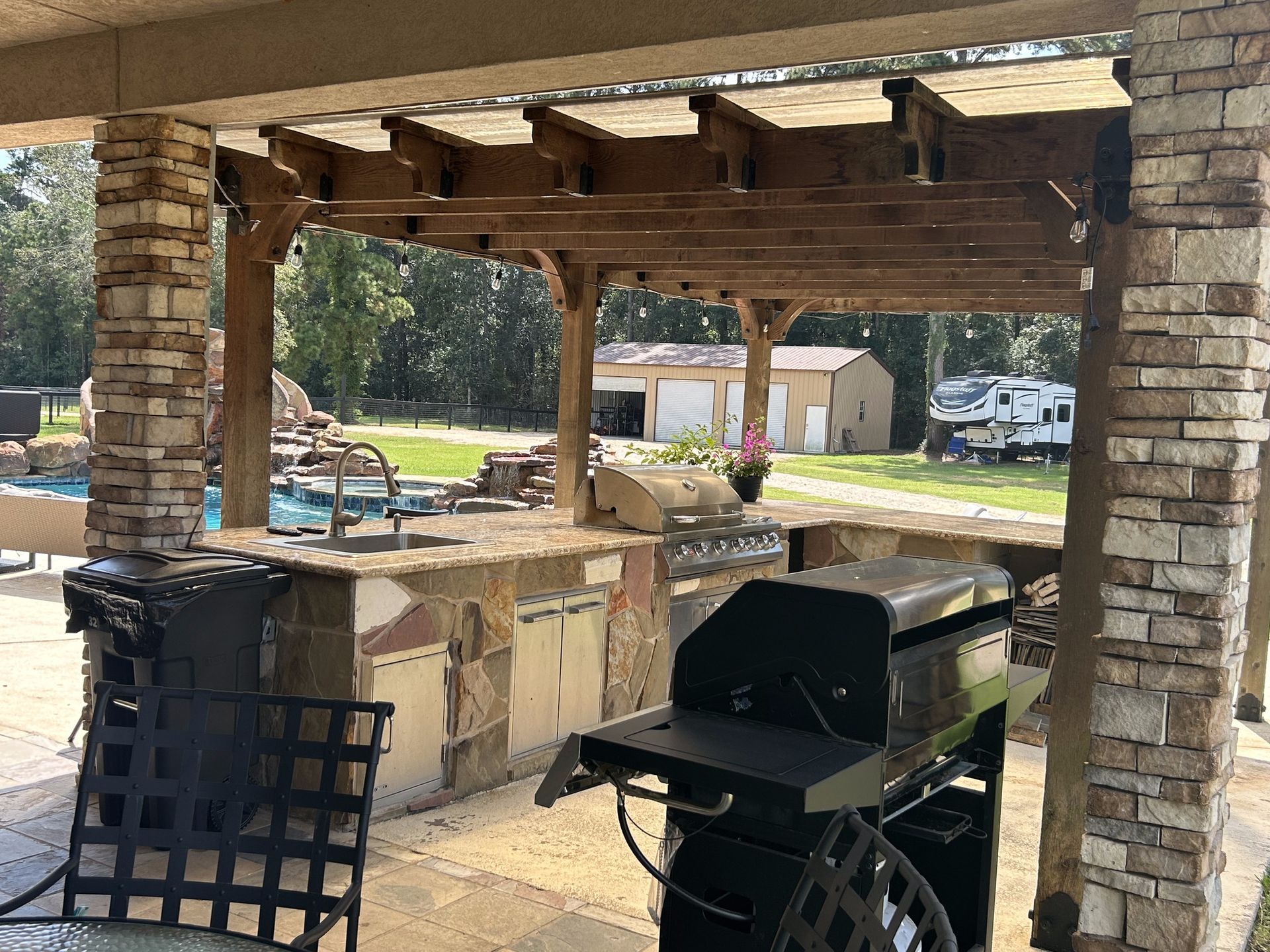 A grill is sitting under a pergola on a patio.