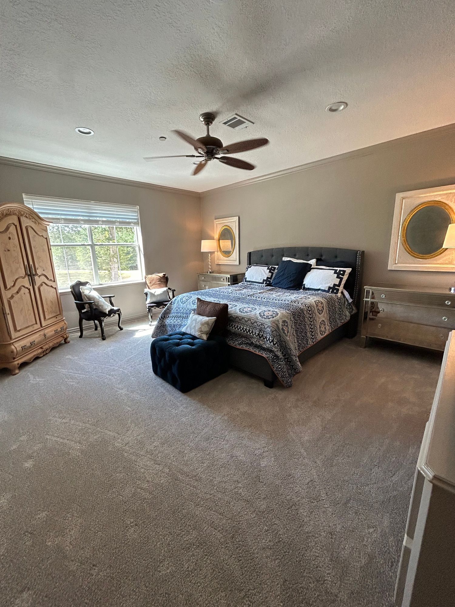 A bedroom with a large bed , ceiling fan , chair and dresser.
